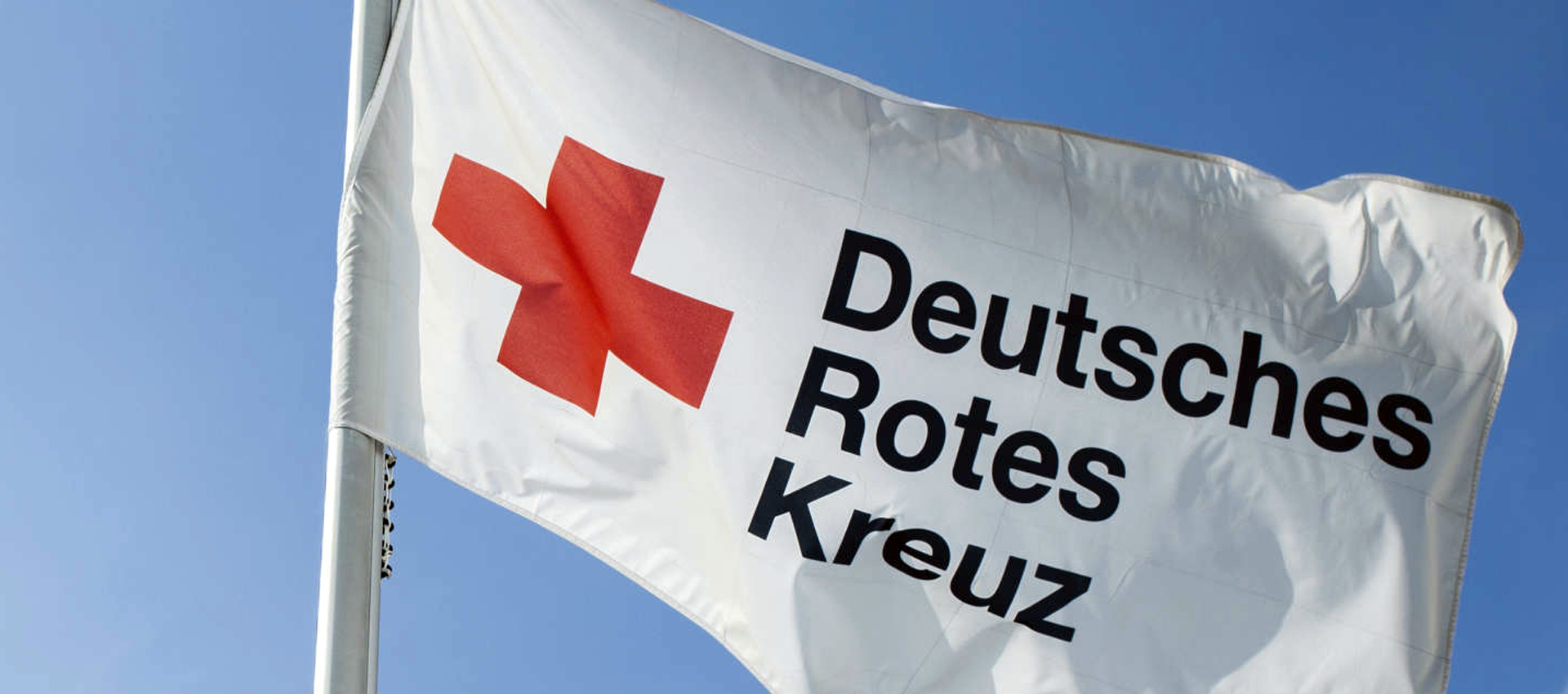 Fahne mit DRK Logo vor blauem Himmel